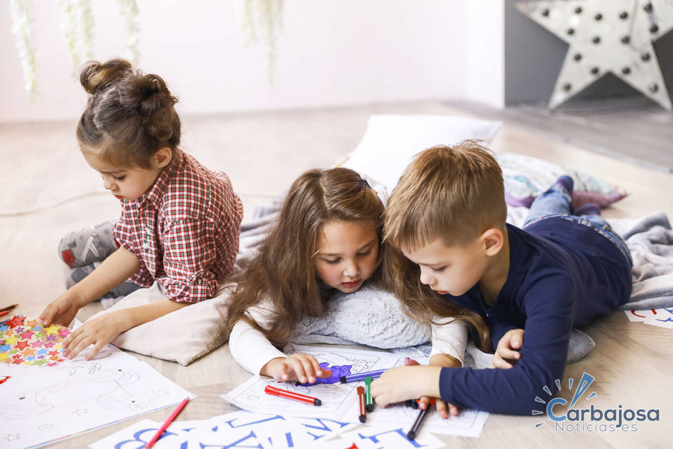 Three focused children are playing on the floor and drawing in coloring books